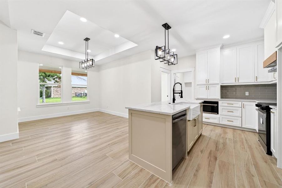 Contemporary kitchen featuring white cabinetry, a large kitchen island with a farmhouse sink, stainless steel appliances, and wood-finish flooring Contemporary kitchen featuring white cabinetry, a large kitchen island with a farmhouse sink, stainless steel appliances, and wood-finish flooring