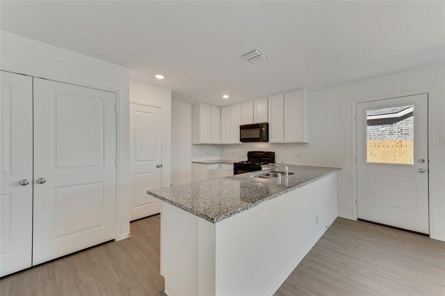 Kitchen with kitchen peninsula, white cabinets, black appliances, and light stone counters