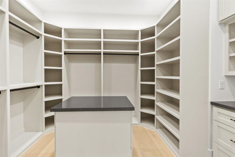 Your custom walk-in closet feels more like a boutique—wraparound built-in shelving, dedicated hanging space, and a sleek center island with a dark countertop keep everything organized and within reach. It’s a thoughtfully designed space that makes getting ready feel effortless and elevated every single day.