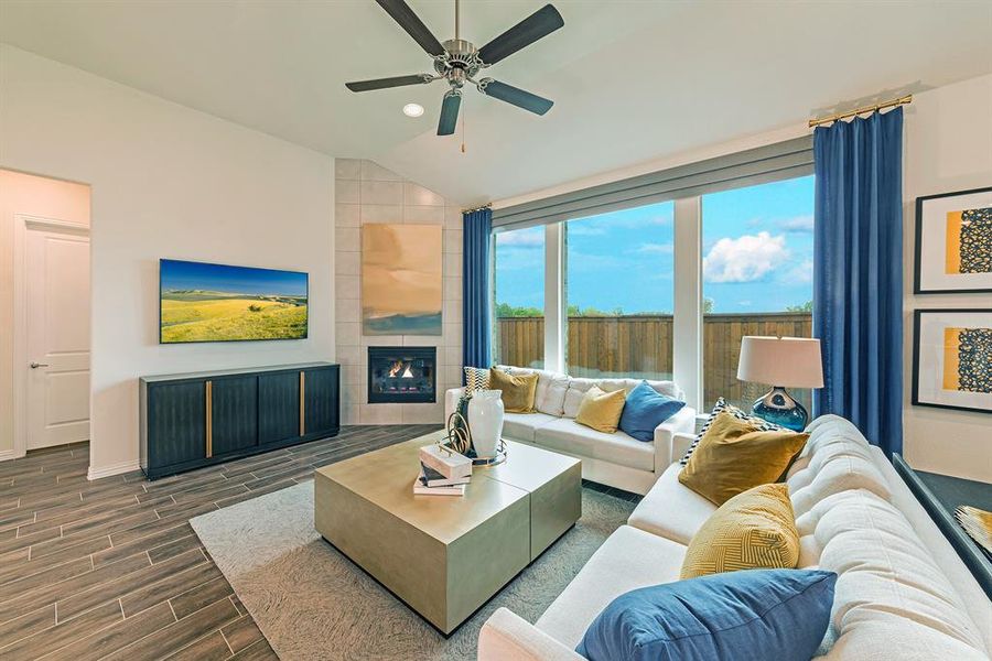Living room featuring a tiled fireplace, wood finish floors, vaulted ceiling, and a ceiling fan