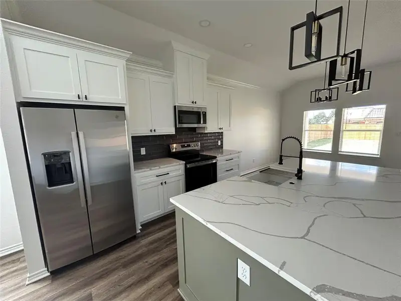 Kitchen with stainless steel appliances, white cabinetry, light stone counters, tasteful backsplash, and dark wood-style floors