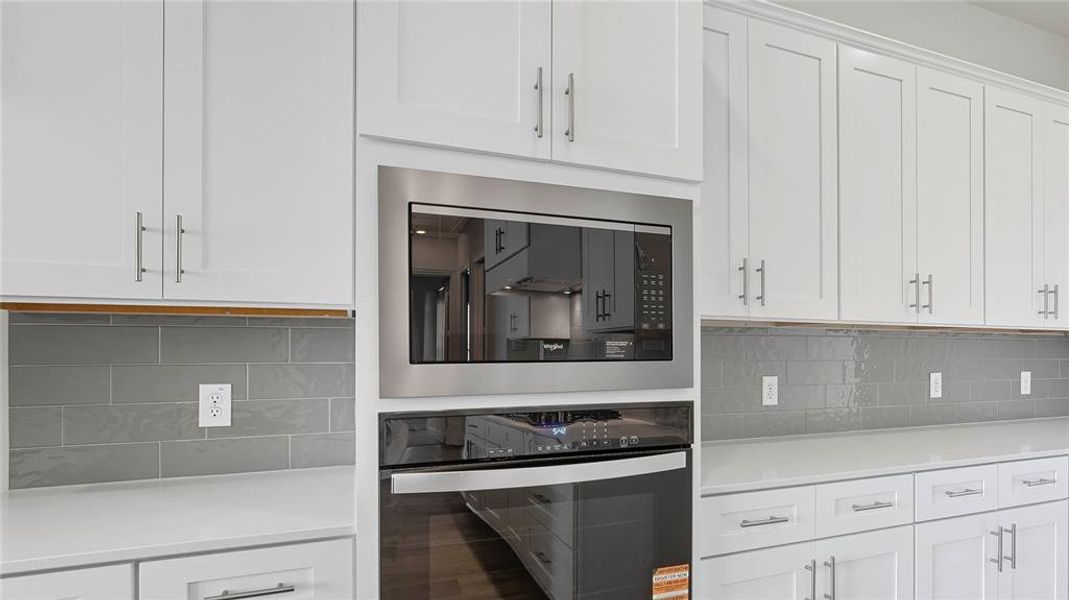 Kitchen featuring white cabinetry, gray subway tile backsplash, stainless steel built-in microwave, stainless steel wall oven, and light-toned countertops