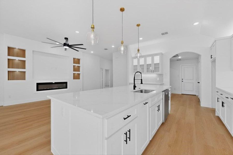 Kitchen featuring white cabinetry, an island with sink, light stone countertops, and arched walkways