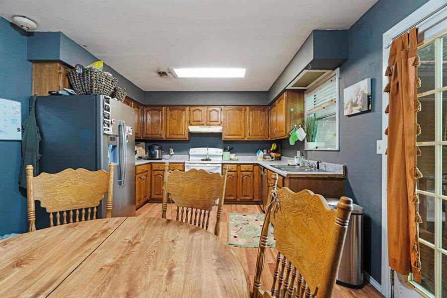 Kitchen featuring light countertops, brown cabinets, electric stove, light wood-style floors, and under cabinet range hood Kitchen featuring light countertops, brown cabinets, electric stove, light wood-style floors, and under cabinet range hood