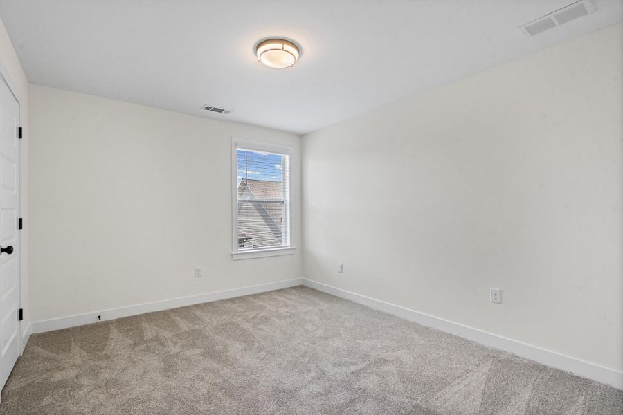 Carpeted room with a single window, white trim, and a flush-mount ceiling light fixture Carpeted room with a single window, white trim, and a flush-mount ceiling light fixture