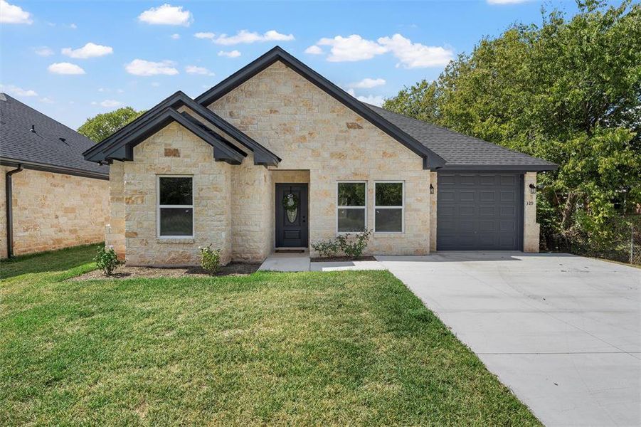 French provincial home featuring a front lawn, driveway, an attached garage, stone siding, and roof with shingles