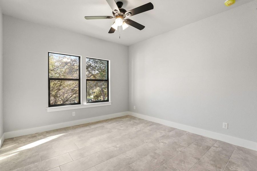 A quiet bedroom featuring tiled flooring and twin windows overlooking verdant trees. A quiet bedroom featuring tiled flooring and twin windows overlooking verdant trees.