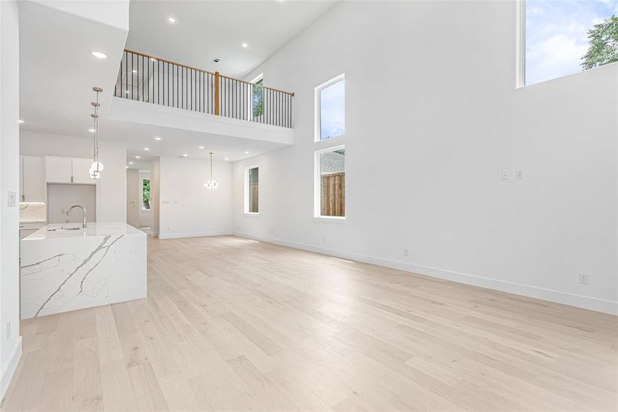 Unfurnished living room featuring light wood-style floors, a towering ceiling, a sink, plenty of natural light, and recessed lighting