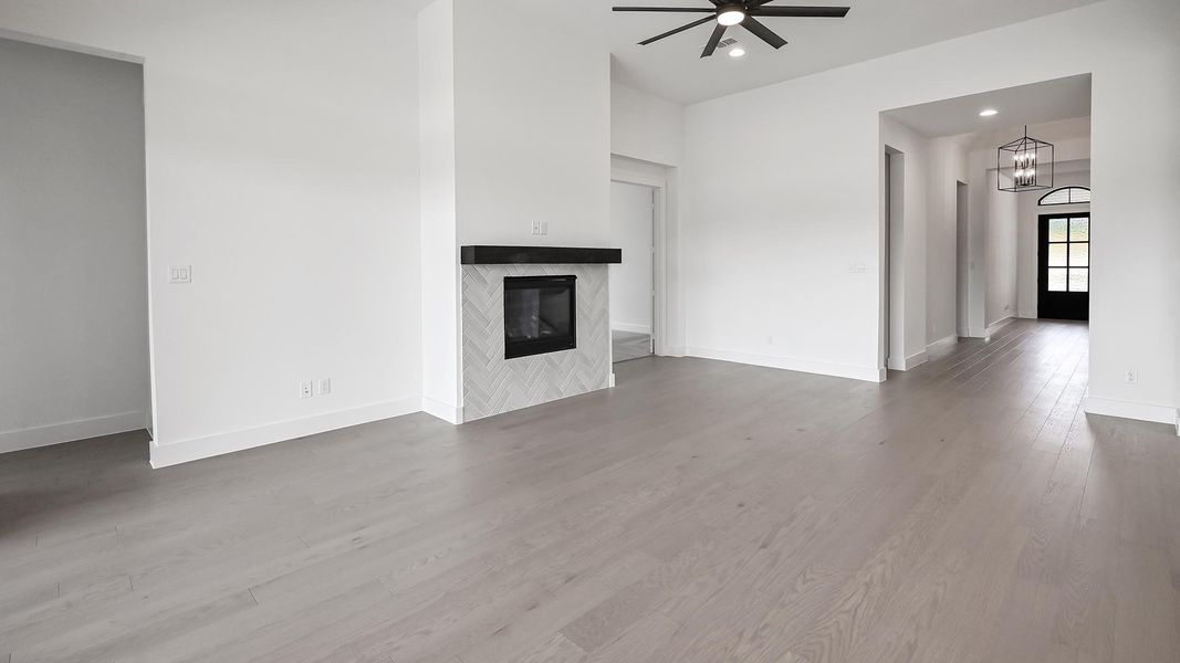Unfurnished living room featuring ceiling fan, a tiled fireplace, wood finished floors, a chandelier, and baseboards