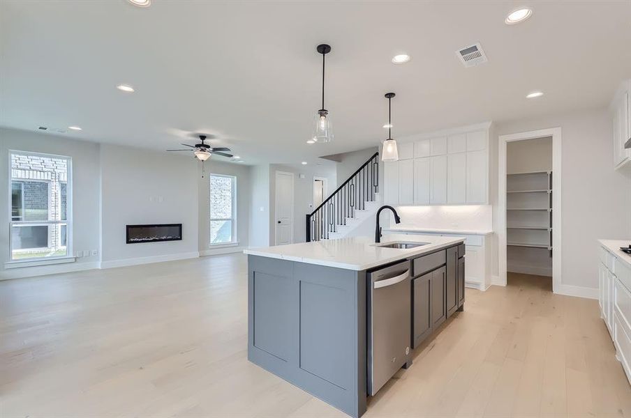 Kitchen with sink, dishwasher, light wood-type flooring, white cabinets, and a kitchen island with sink