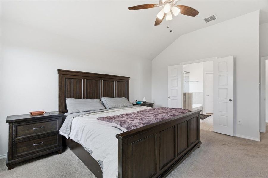 Bedroom featuring light carpet, vaulted ceiling, a ceiling fan, and connected bathroom