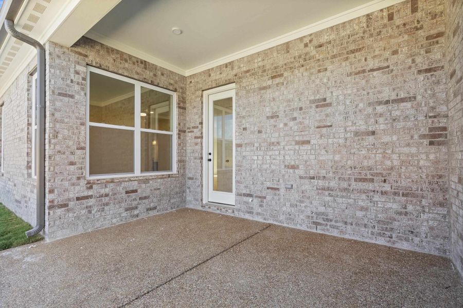 Covered patio featuring aggregate concrete flooring, full-brick exterior walls, and a multi-pane glass door Covered patio featuring aggregate concrete flooring, full-brick exterior walls, and a multi-pane glass door