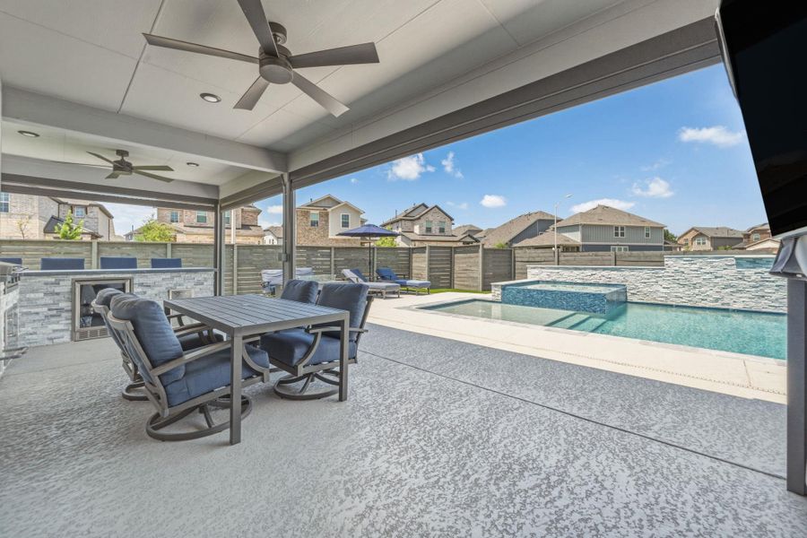 Covered patio featuring an outdoor kitchen with integrated beverage cooler, dual ceiling fans, and textured cool coat concrete flooring