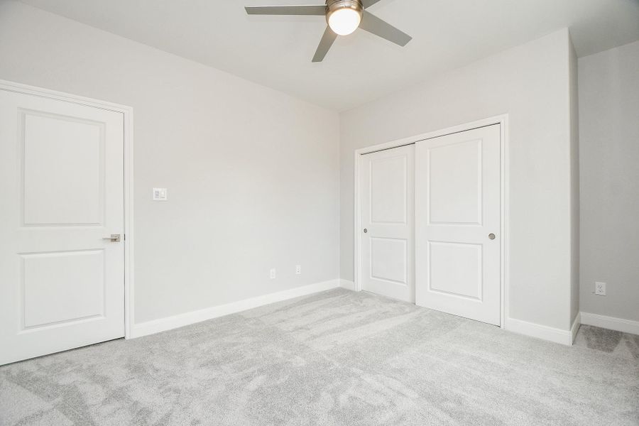 This is a clean, secondary  bedroom featuring plush carpeting, neutral walls, a ceiling fan, and a double-door closet providing ample storage.