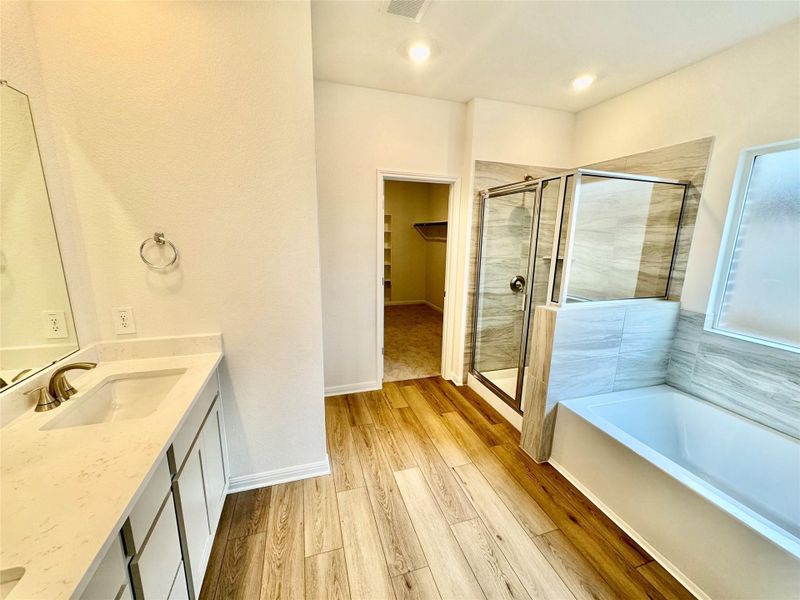 Bathroom featuring double vanity, a spacious closet, a shower stall, a garden tub, and light wood-style floors