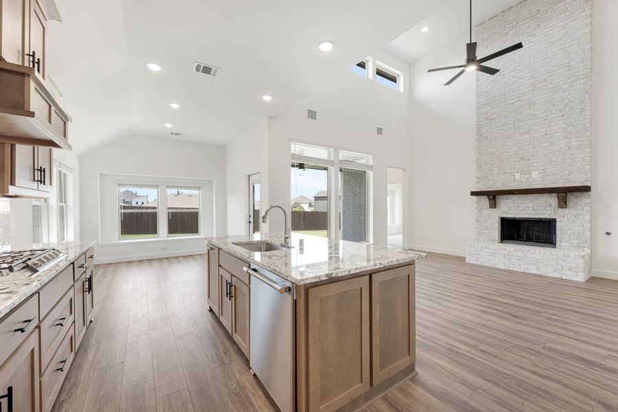 Open kitchen with center island, granite countertops, and wood cabinets, open to living room with stone fireplace and vaulted ceiling Open kitchen with center island, granite countertops, and wood cabinets, open to living room with stone fireplace and vaulted ceiling