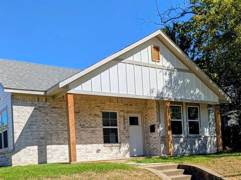 View of front facade featuring covered porch, board and batten siding, brick siding, a front yard, and roof with shingles