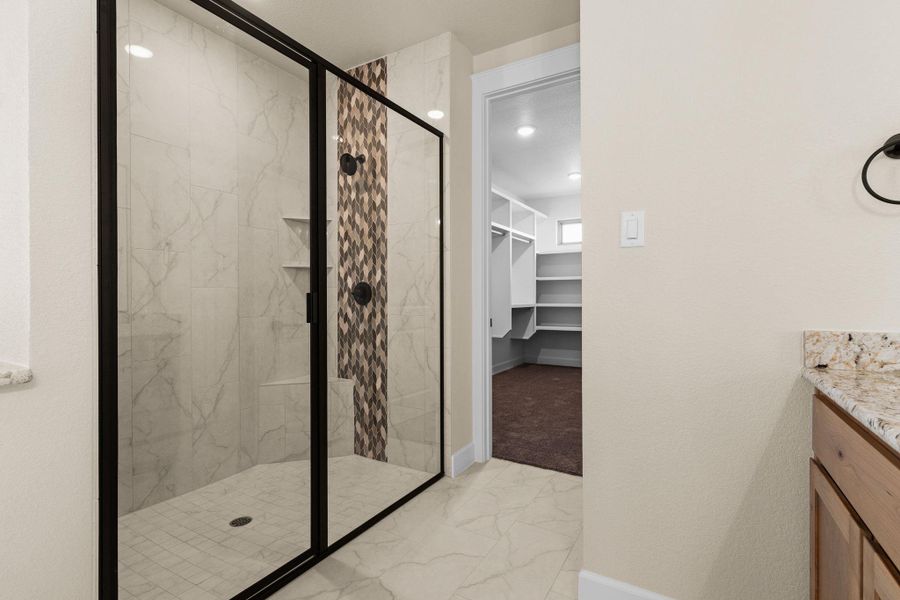 Bathroom featuring a marble finish shower, vanity, light marble finish floors, and a walk in closet Bathroom featuring a marble finish shower, vanity, light marble finish floors, and a walk in closet