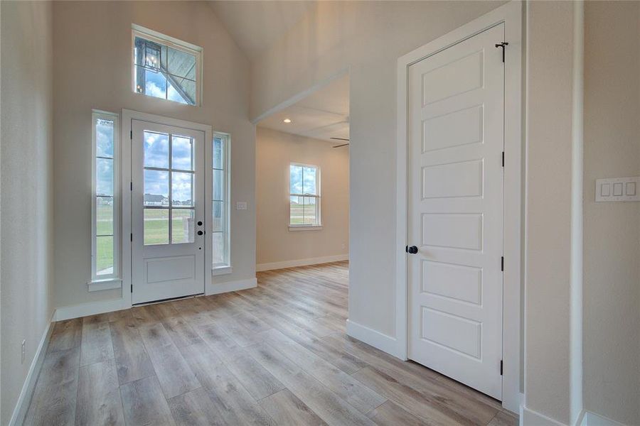 Foyer entrance with high vaulted ceiling, ceiling fan, and light hardwood / wood-style flooring