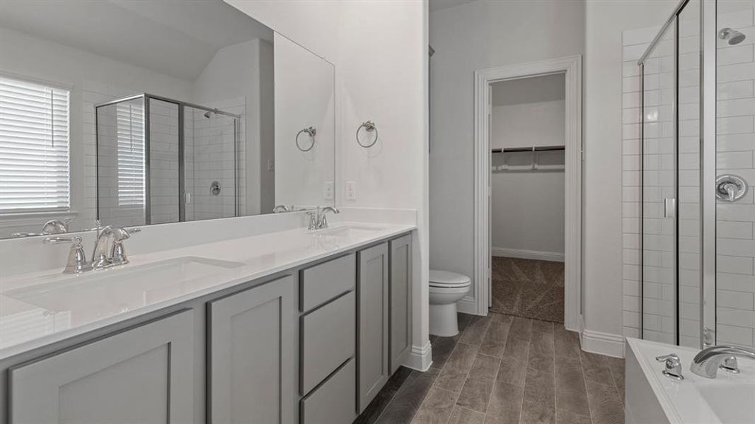 Full bath with a spacious closet, double vanity, a shower stall, wood finish floors, and a bath