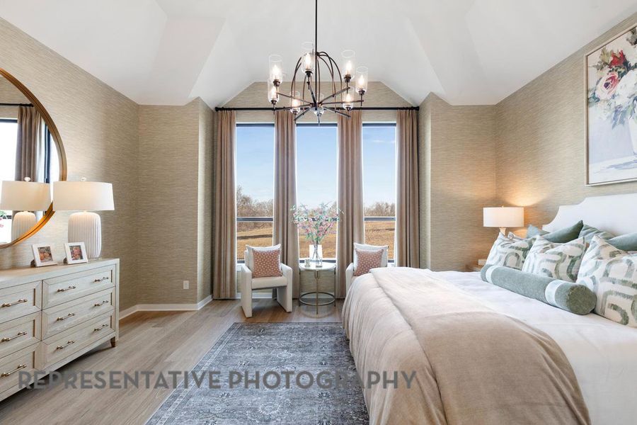 Bedroom with wallpapered walls, light wood-style flooring, lofted ceiling, a chandelier, and baseboards