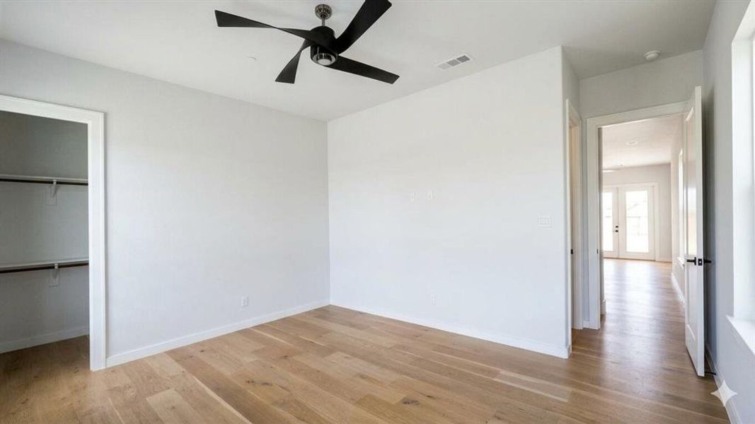 Spacious room featuring wood-finish flooring, a modern ceiling fan, and a walk-in closet with shelving