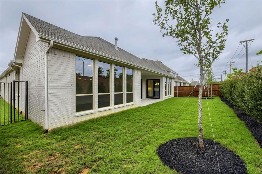 The property features an extensive green lawn with a young tree, a paved patio area, and large windows along the exterior wall