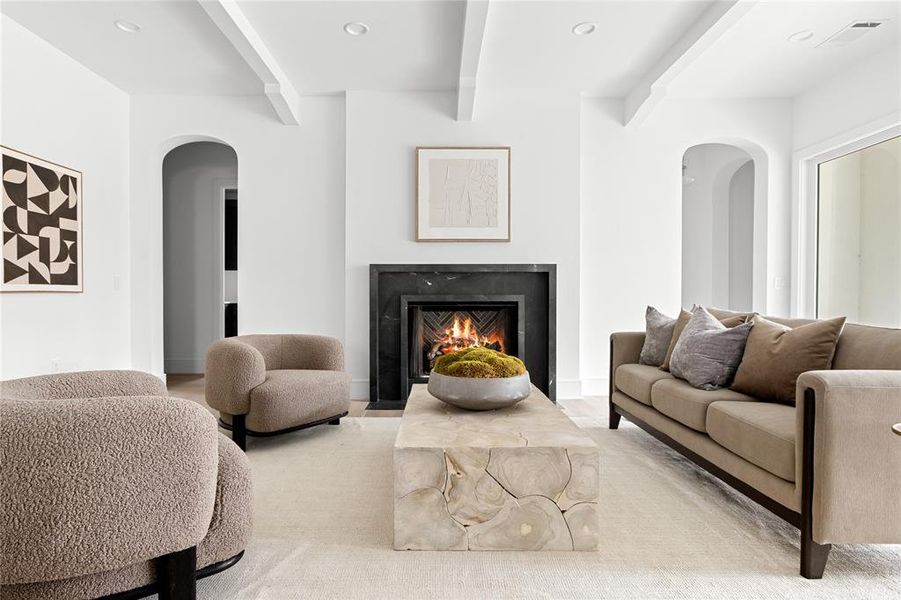 Living area featuring arched walkways, recessed lighting, a fireplace with flush hearth, and beamed ceiling