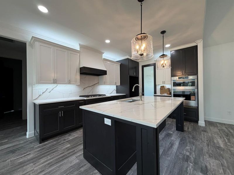 Gourmet kitchen featuring a large central island with a sink, stainless steel appliances, two-tone cabinetry, wood-finish flooring, and pendant lighting