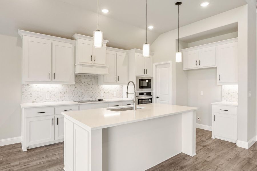 White kitchen with center island, pendant lights, stainless steel appliances, and tile backsplash on wood-look floors White kitchen with center island, pendant lights, stainless steel appliances, and tile backsplash on wood-look floors