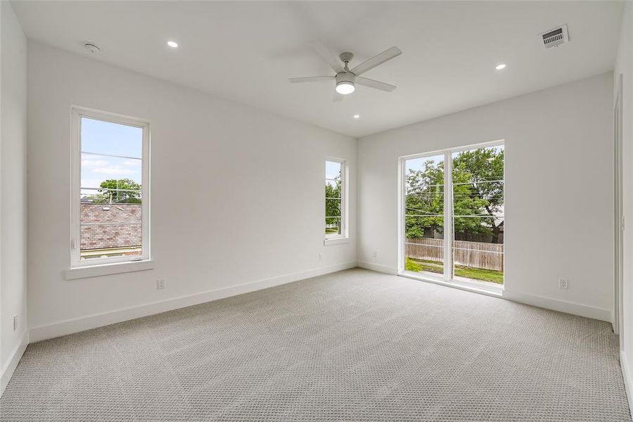 Carpeted room featuring a ceiling fan with integrated lighting, recessed lighting, white walls, and multiple windows including a large sliding glass door