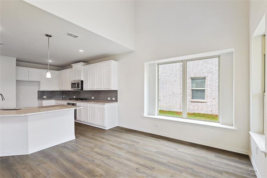 Kitchen with light wood-type flooring, white cabinets, pendant lighting, and sink