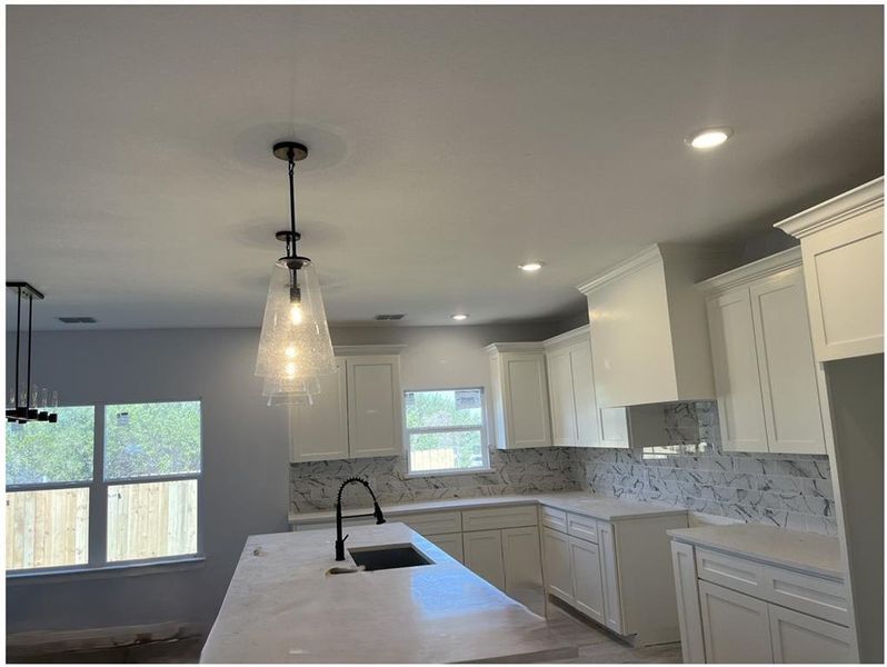 Kitchen with sink, decorative light fixtures, light wood-type flooring, white cabinets, and tasteful backsplash