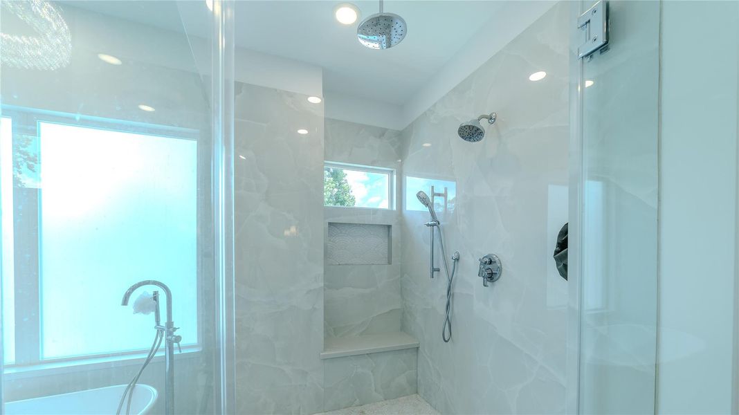 This bathroom features a modern shower with marble-style tiles, dual showerheads, and a built-in bench. It also has a frosted glass window for natural light and privacy.