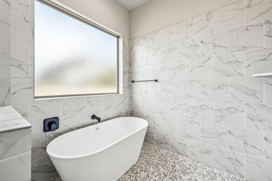 Bathroom with tile walls, a bathing tub, and a healthy amount of sunlight