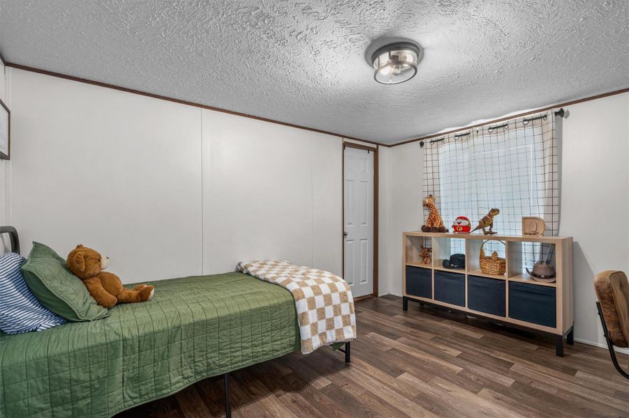 Bedroom featuring ornamental molding, dark wood-type flooring, a textured ceiling, and a decorative wall