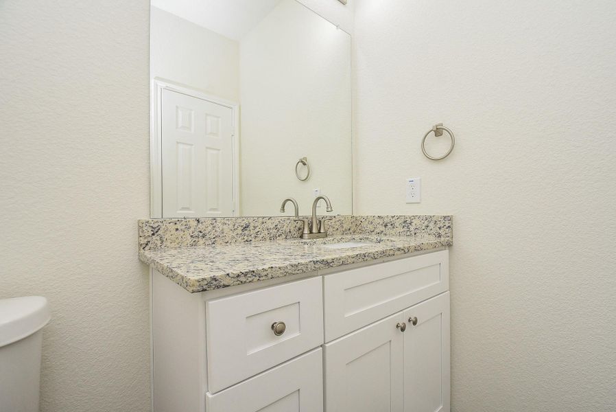 A clean, modern bathroom with a white vanity cabinet, granite countertop, undermount sink, framed mirror, and towel ring on a textured wall. A clean, modern bathroom with a white vanity cabinet, granite countertop, undermount sink, framed mirror, and towel ring on a textured wall.