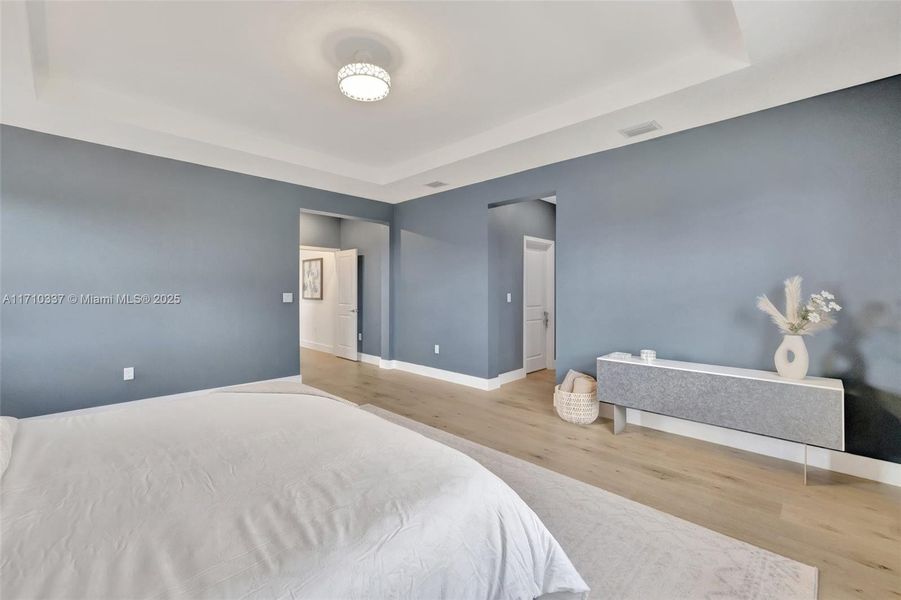 Primary Bedroom w/ view toward double door entry and office, and to the right are dual walk in closets and oversized en suite bathroom