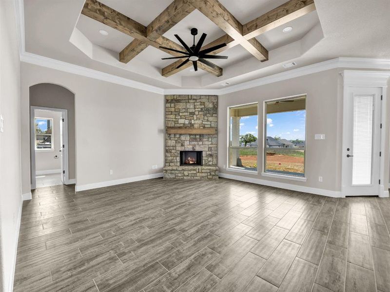 Unfurnished living room with a stone fireplace, arched walkways, coffered ceiling, and wood finish floors Unfurnished living room with a stone fireplace, arched walkways, coffered ceiling, and wood finish floors