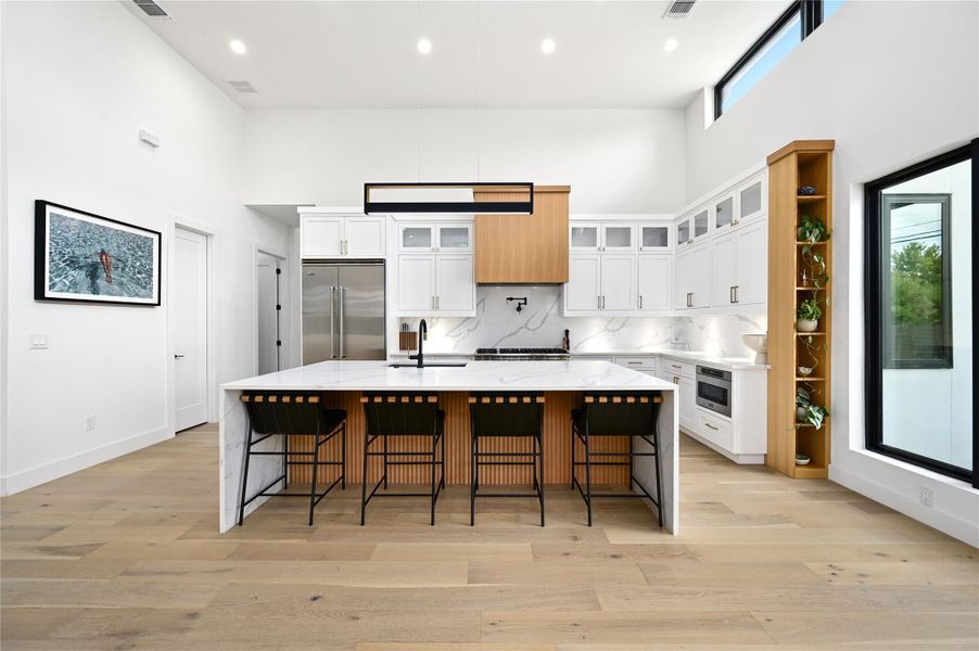 Kitchen with white cabinetry, a high ceiling, light wood-style flooring, and built in appliances