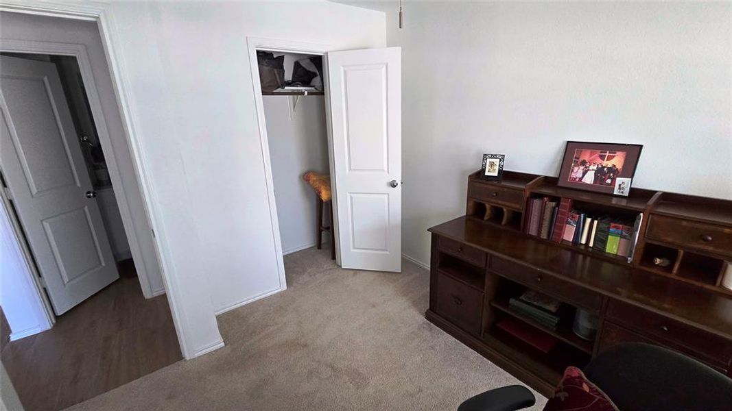 Carpeted room featuring a white paneled door, a built-in closet with a shelf, and wood-finish flooring visible through an open doorway