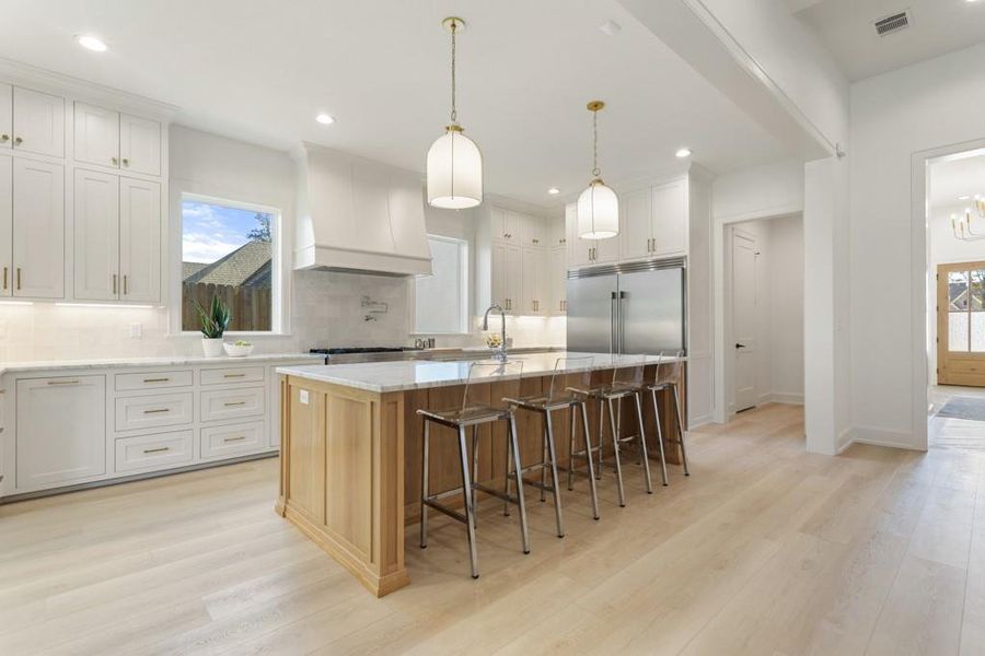 Kitchen featuring white cabinetry, light stone counters, hanging light fixtures, a breakfast bar, and premium range hood