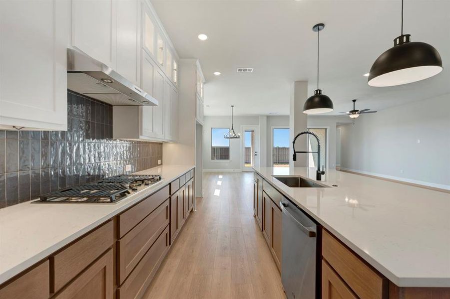 Kitchen featuring light wood-style flooring, pendant lighting, two tone cabinetry, stainless steel appliances, and light stone countertops