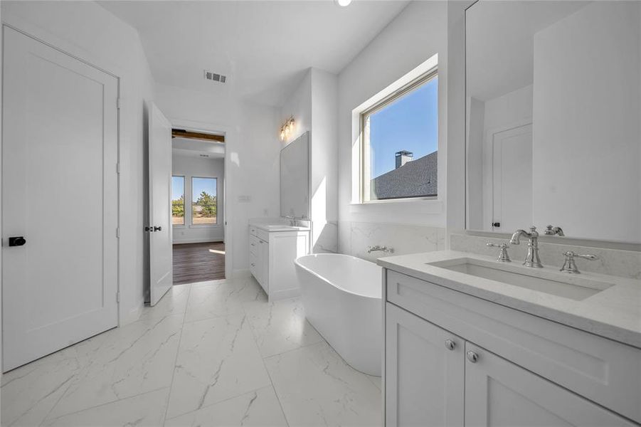 Bathroom featuring two vanities, a soaking tub, and light marble finish flooring
