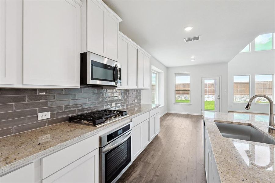 Kitchen featuring backsplash, light stone counters, dark hardwood / wood-style floors, stainless steel appliances, and sink