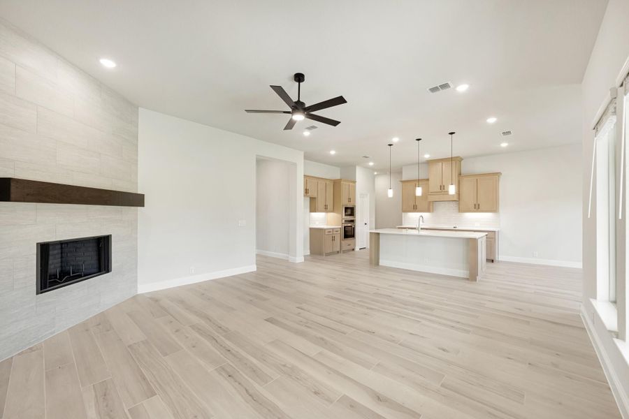 Open living area with tile fireplace and ceiling fan, open to kitchen with island and light wood cabinets
