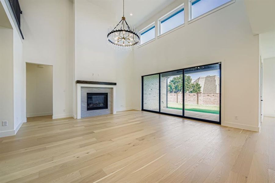 Unfurnished living room featuring light wood-style flooring, a towering ceiling, a chandelier, and a tiled fireplace Unfurnished living room featuring light wood-style flooring, a towering ceiling, a chandelier, and a tiled fireplace