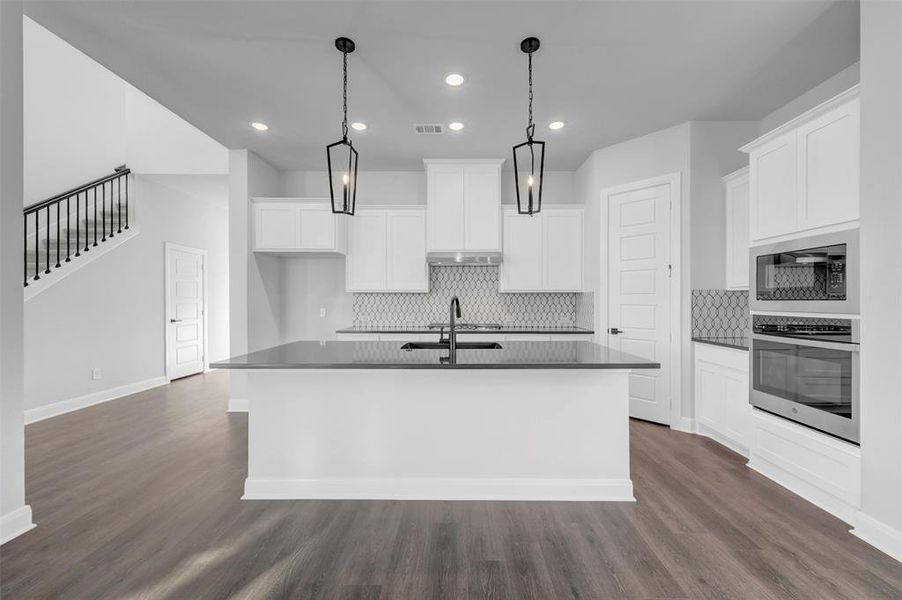Kitchen featuring stainless steel appliances, an island with sink, dark wood-style flooring, white cabinetry, and tasteful backsplash Kitchen featuring stainless steel appliances, an island with sink, dark wood-style flooring, white cabinetry, and tasteful backsplash