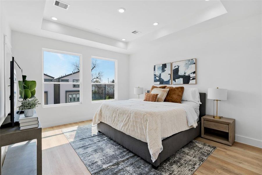 The primary bedroom boasts a soaring trey ceiling and oversized windows, creating a serene retreat flooded with natural light and elevated by elegant architectural details.