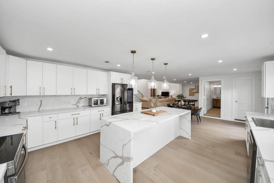 Stunning waterfall island with seating and pendant lighting. The kitchen flows seamlessly into the open-concept living and dining area, perfect for entertaining. Stunning waterfall island with seating and pendant lighting. The kitchen flows seamlessly into the open-concept living and dining area, perfect for entertaining.